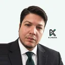 Retrato de César Ávila, con traje gris oscuro y corbata verde, sobre fondo claro con el logo de Klinoda